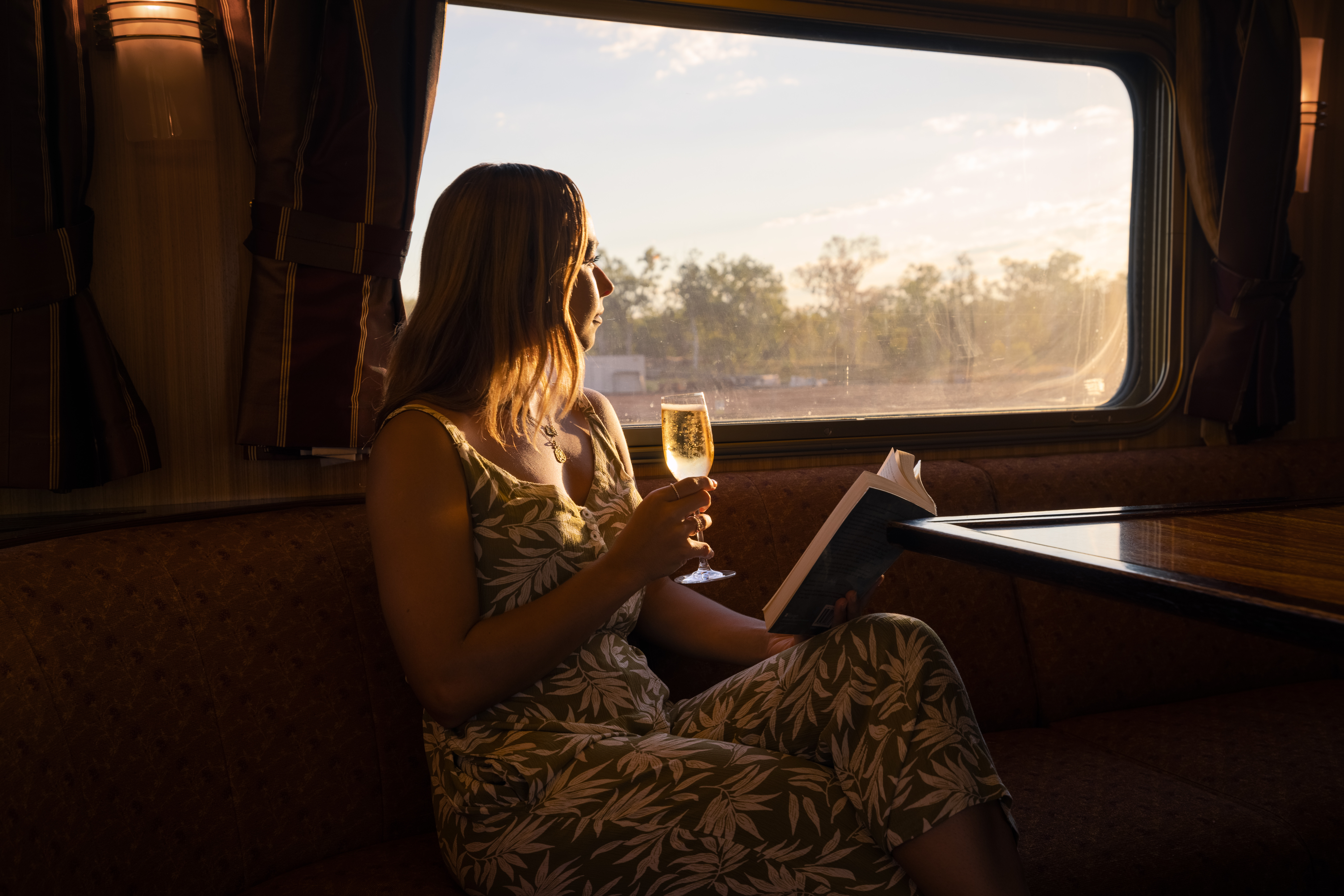 Woman enjoying a drink and a book onboard the Ghan